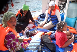 مهاجرات مع أطفالهن على سطح سفينة دورية بعد ان تم إنقاذهم من البحر