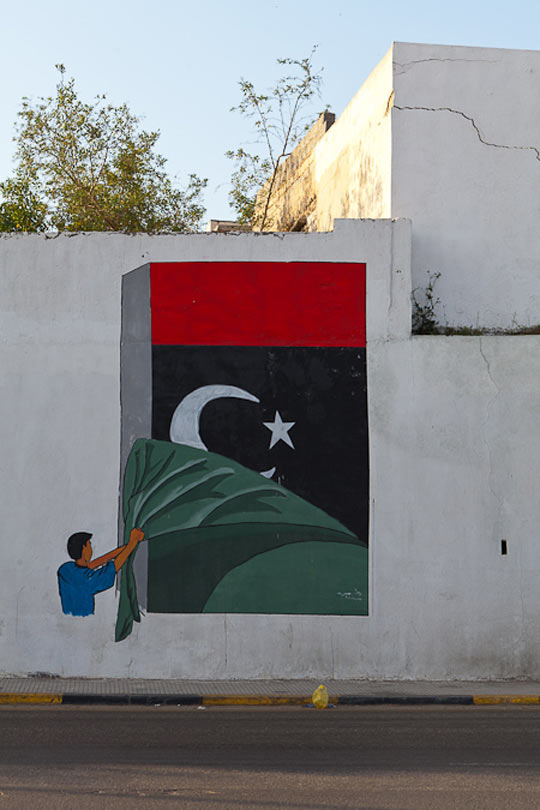 //An ever-present motif on the streets: the restored pre-Gaddafi red-green-black flag. In this Tripoli mural, the green Jamahariya flag is ripped down to reveal the new banner behind it.
