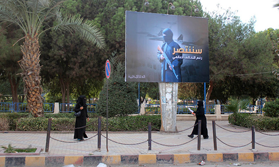 //Women wearing a niqab, a type of full veil, walk under a billboard erected by the Islamic State (IS) group as part of a campaign in the IS controlled Syrian city of Raqqa on November 1, 2014. Arabic writting on billboard "We shall be triumphant, in spite of the global coalition". AFP PHOTO/RMC/STR