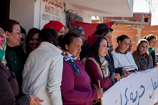 //Le operaie davanti alla Mamotex chiusa, afferrano uno striscione che rivendica il loro diritto al lavoro, sopra di loro la bandiera dell’UGTT (l’Union Générale des Travailleurs Tunisiens), il potente sindacato dei lavoratori tunisini. Foto di Monia Ben Hamadi.