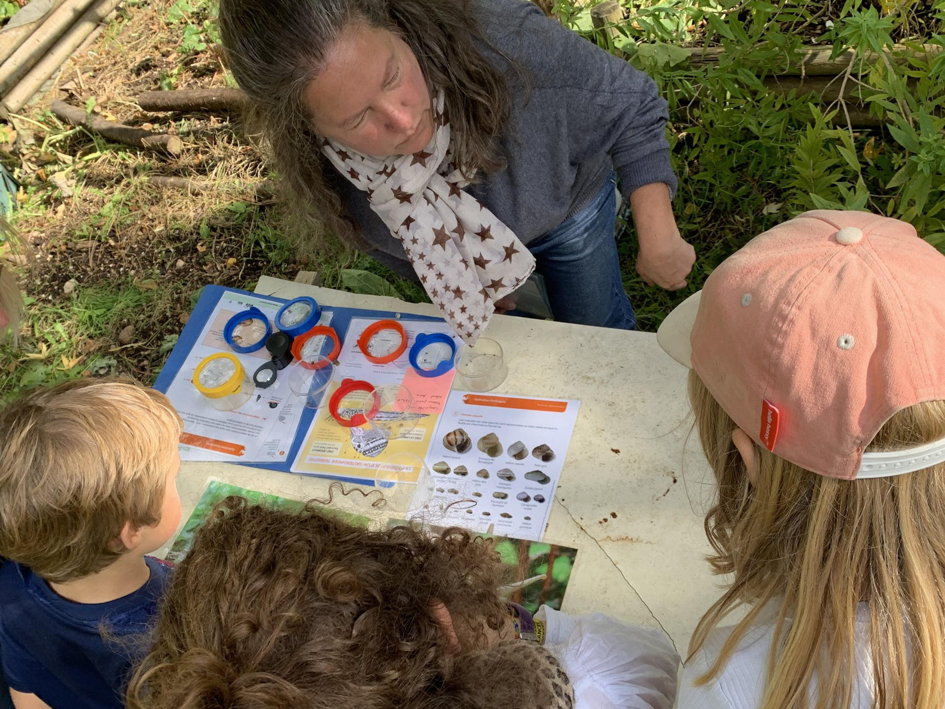 Des enfants observent les escargots du jardin avec une animatrice