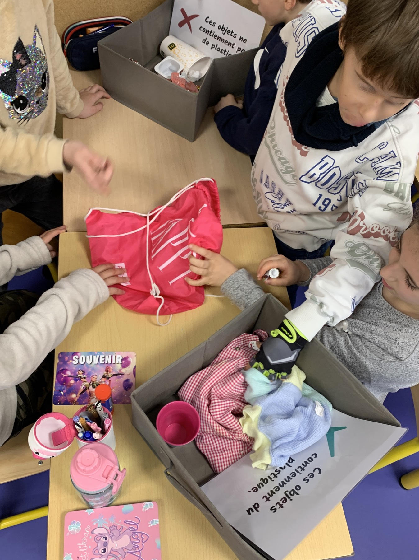 Des enfants trient des objets du quotidien dans deux boîtes, avec ou sans plastique