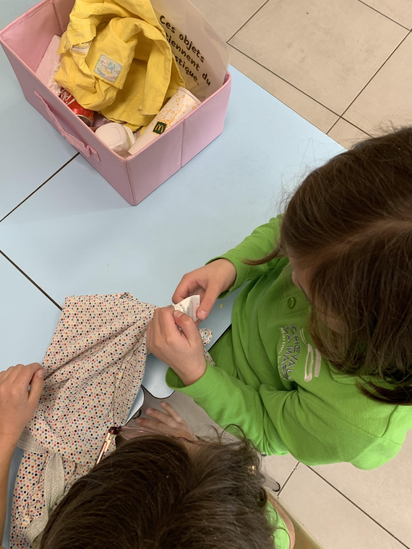 Vue du dessus : des enfants examinent des vêtements et des objets près d'une boîte « Ces objets contiennent du plastique »